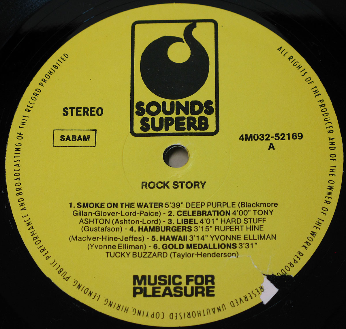 Close-up of the yellow Sounds Superb label for the Belgian compilation album Rock Story, pressed by EMI Music For Pleasure. The label is circular with a bold black Sounds Superb logo at the top, showing a stylized record groove forming an 'S'. The catalog number 4M032-52169 A is printed on the right, with 'STEREO' and the SABAM rights society mark on the left. The album title Rock Story appears centered above the track listing for Side A, printed in black. Tracks listed are: 1. Smoke on the Water – Deep Purple (5:39), 2. Celebration – Tony Ashton (4:00), 3. Libel – Hard Stuff (4:01), 4. Hamburgers – Rupert Hine (3:15), 5. Hawaii – Yvonne Elliman (3:14), and 6. Gold Medallions – Tucky Buzzard (3:31). Below the listing is the Music for Pleasure imprint. The outer rim carries the copyright and broadcasting restrictions text. A small chip is visible on the label’s edge near the runout groove.