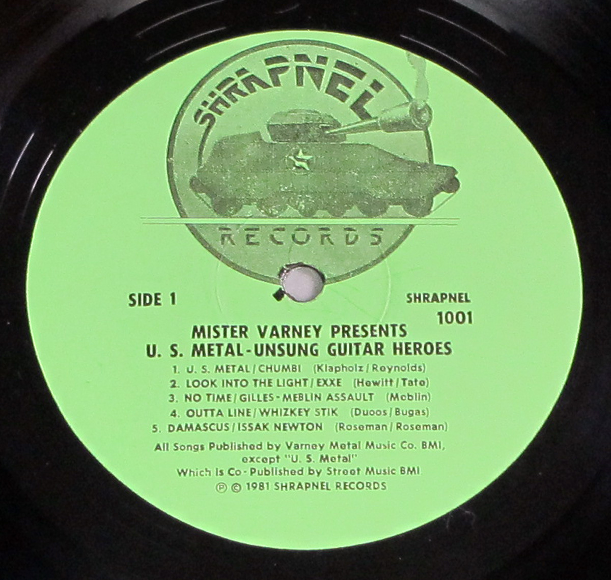 Green Shrapnel Records label for U.S. Metal - Unsung Guitar Heroes, featuring a tank logo at the top and tracklist details for Side 1, including five songs and publishing credits. Released in 1981 with catalog number Shrapnel 1001.