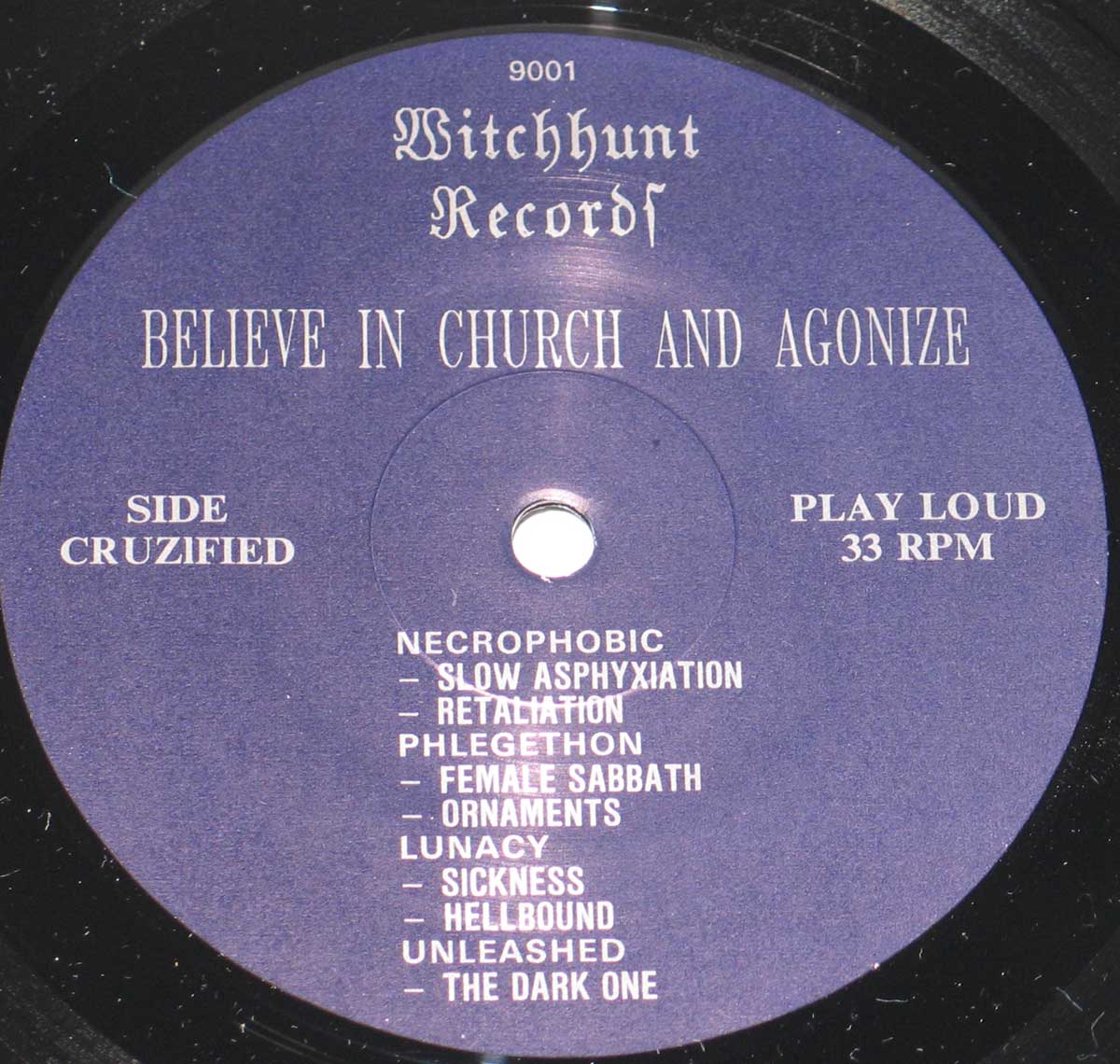 Record label for the album “Believe in Church and Agonize” by Witchhunt Records featuring a purple background with white Gothic and serif text. The label includes the album title, catalog number “9001,” “Side Cruzified,” “Play Loud,” and “33 RPM.” The tracklist includes titles such as “Slow Asphyxiation,” “Female Sabbath,” and “The Dark One.”